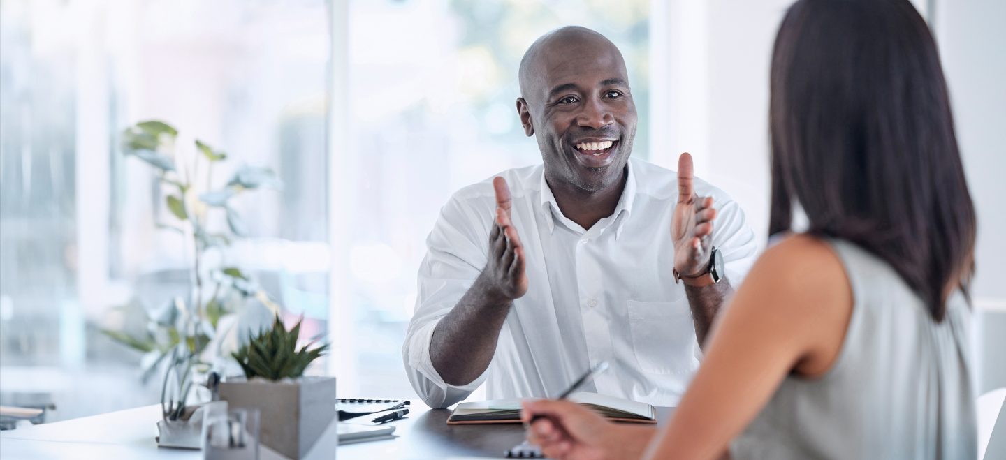 Man speaking animatedly while working at a table with his coworkers. A 54 out of 60 scale and a purple ‘Enable Others to Act’ leadership behavior banner are in the bottom right corner.