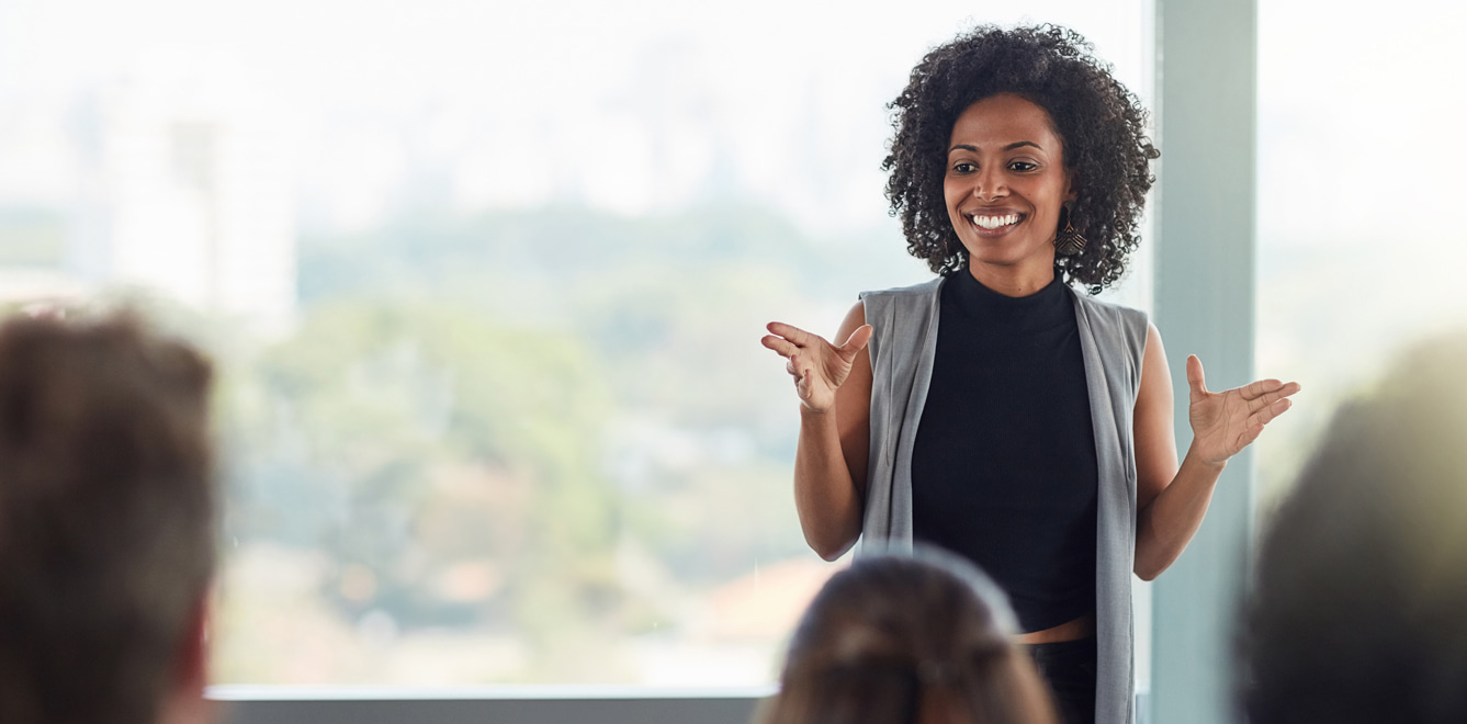 Smiling woman presenting to a group, with a 56 out of 60 scale and a blue ‘Inspire a Shared Vision’ leadership behavior banner in the bottom right corner.